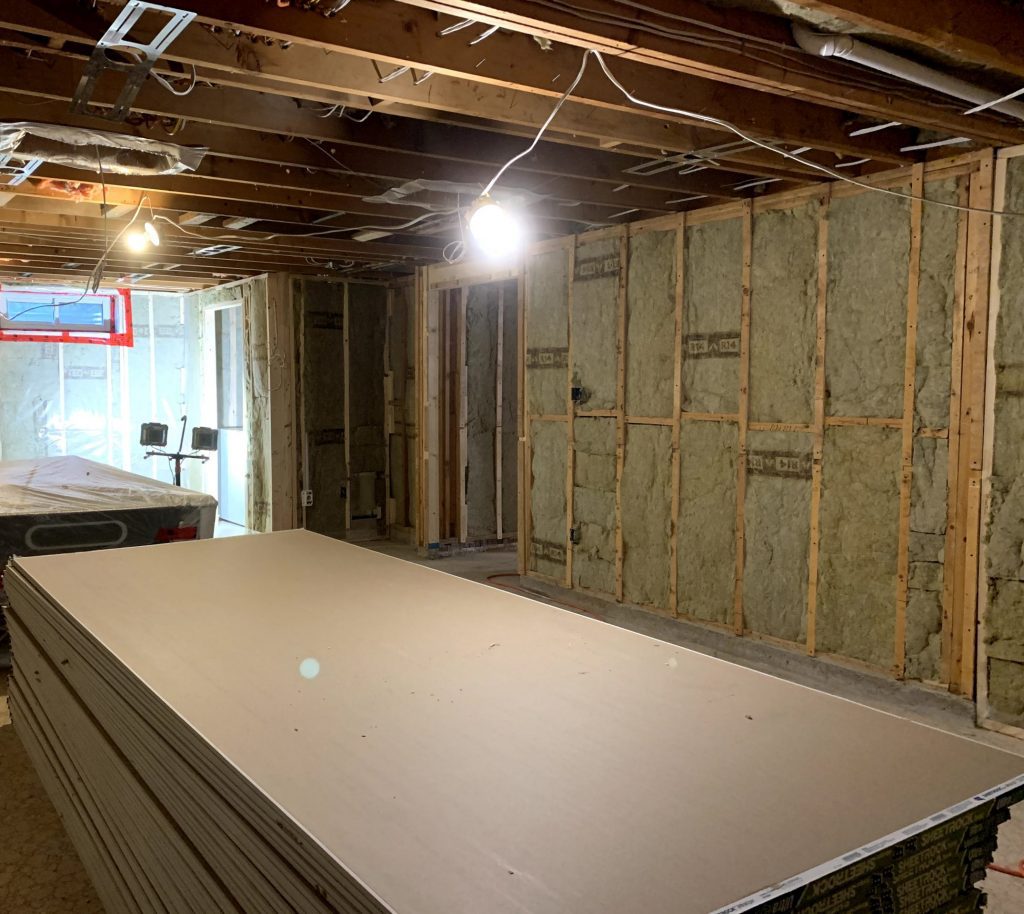 Framed basement wall with pile of drywall waiting for installation.